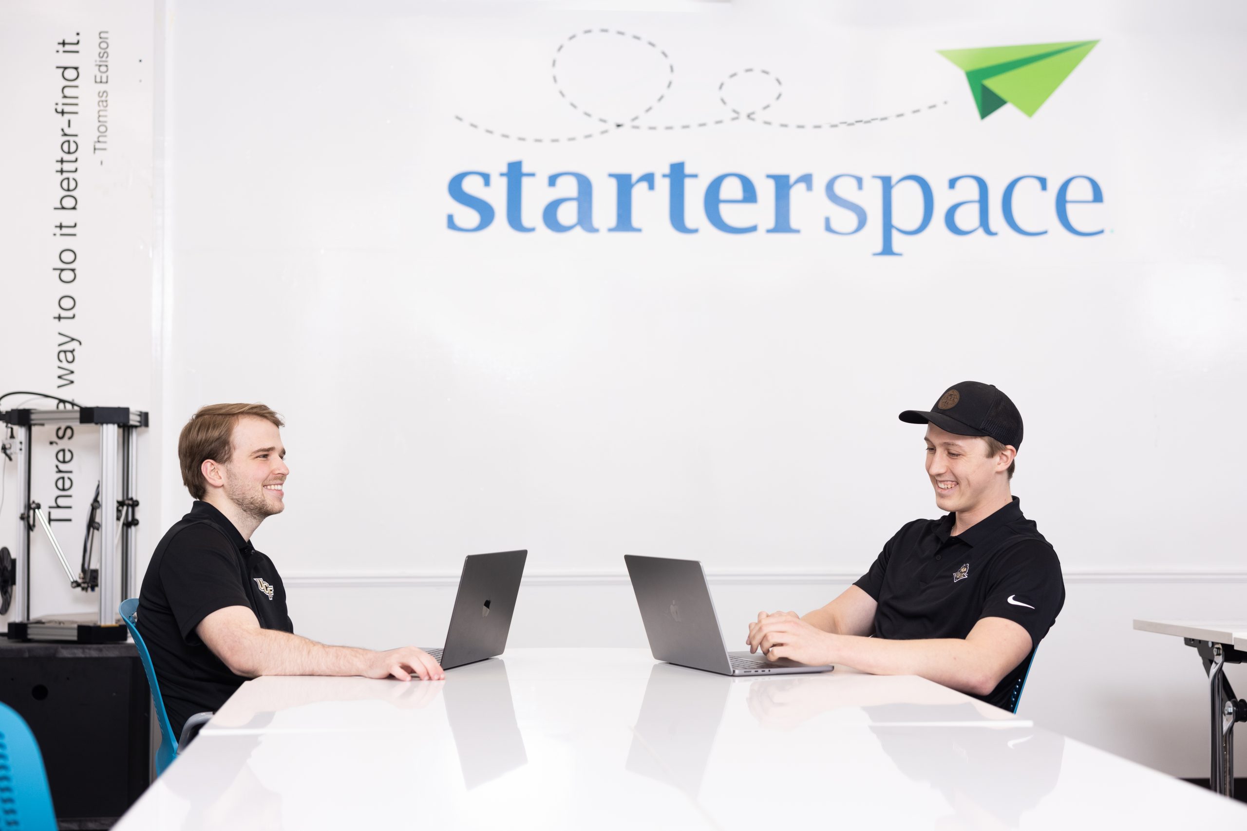 two students in black polos in front of laptops seated at a white table